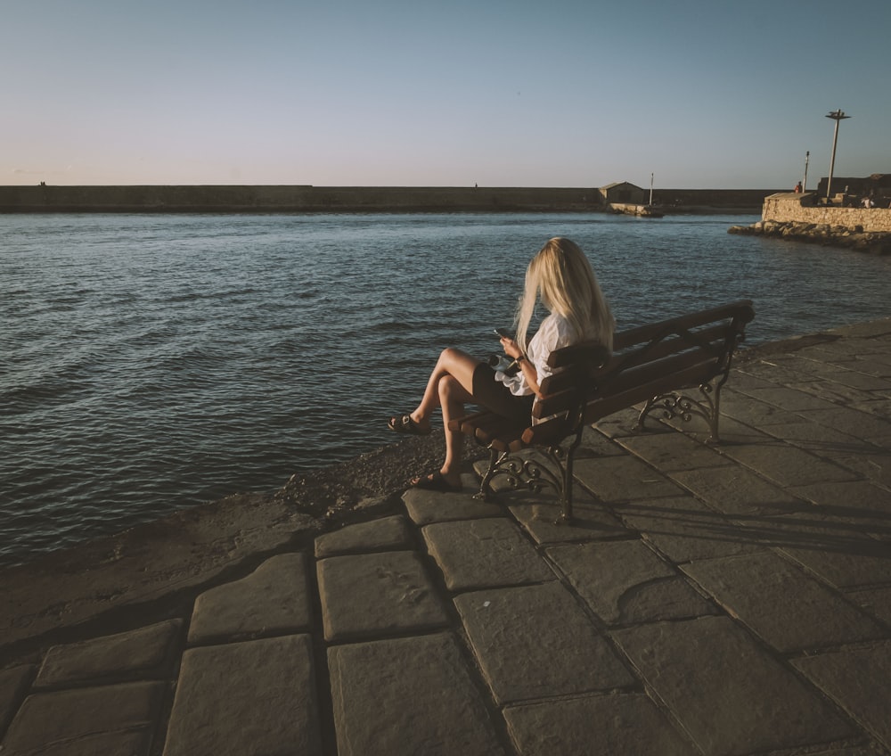 a person sitting on a bench next to a body of water