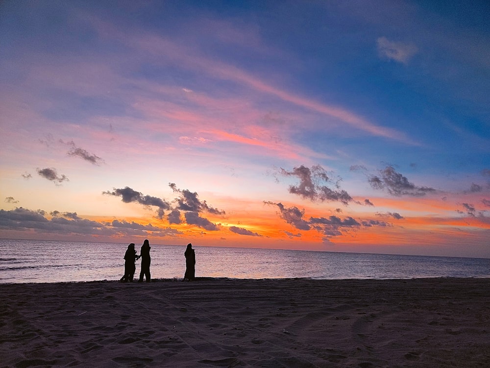 a group of people standing on a beach during sunset