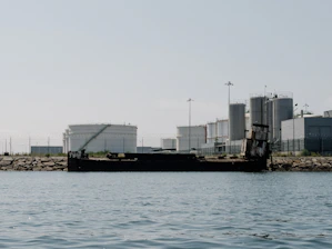 A panoramic view of heavy-oil storage tanks at a coastal refinery under a clear sky.