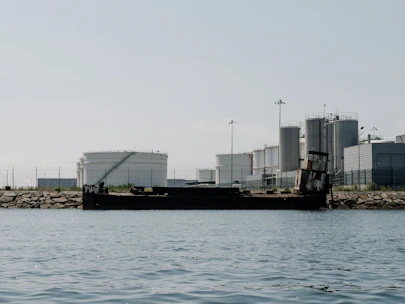 A panoramic view of heavy-oil storage tanks at a coastal refinery under a clear sky.
