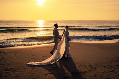 Bride and groom walking hand in hand along a quiet beach at sunset.