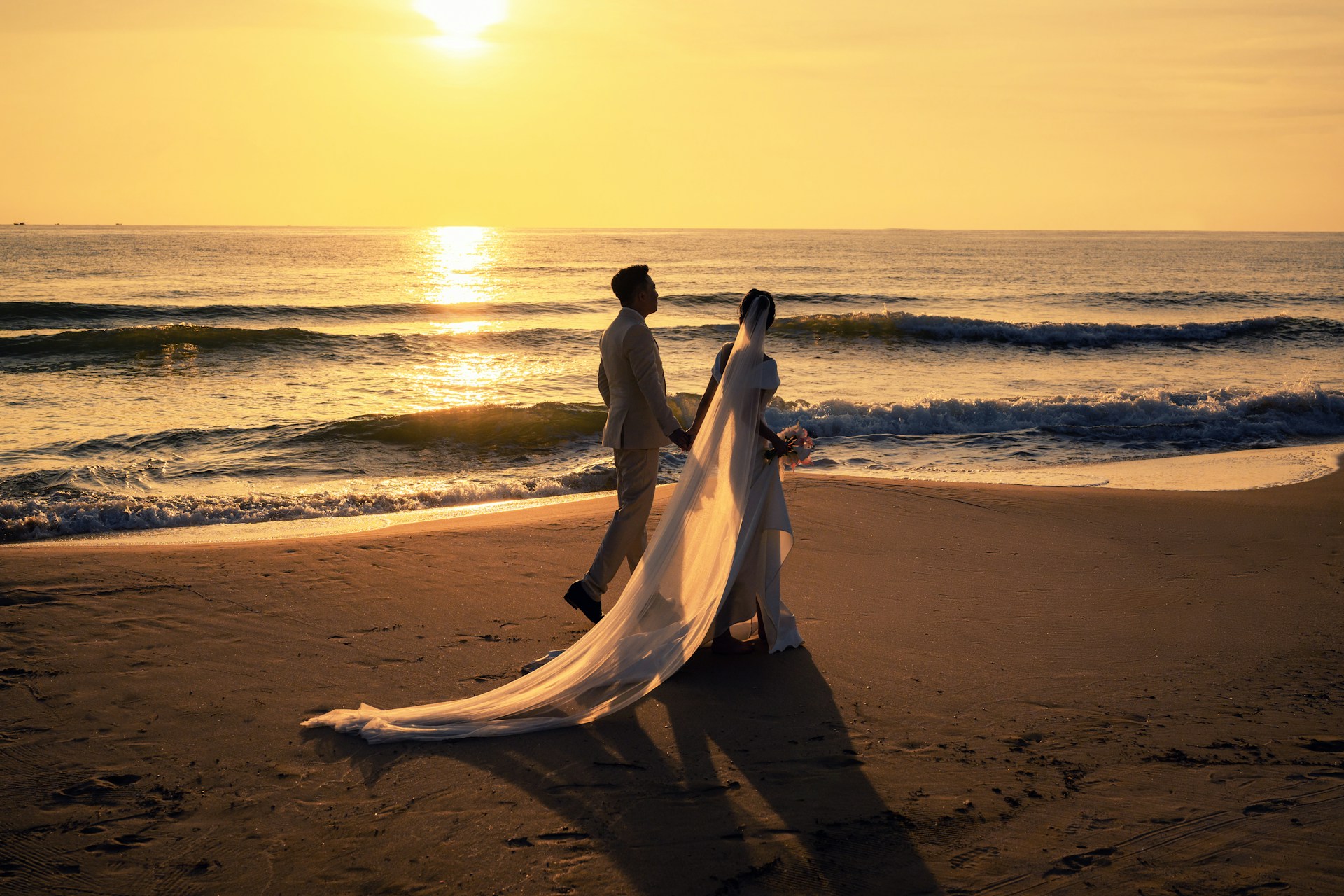 a bride and groom walking down the beach