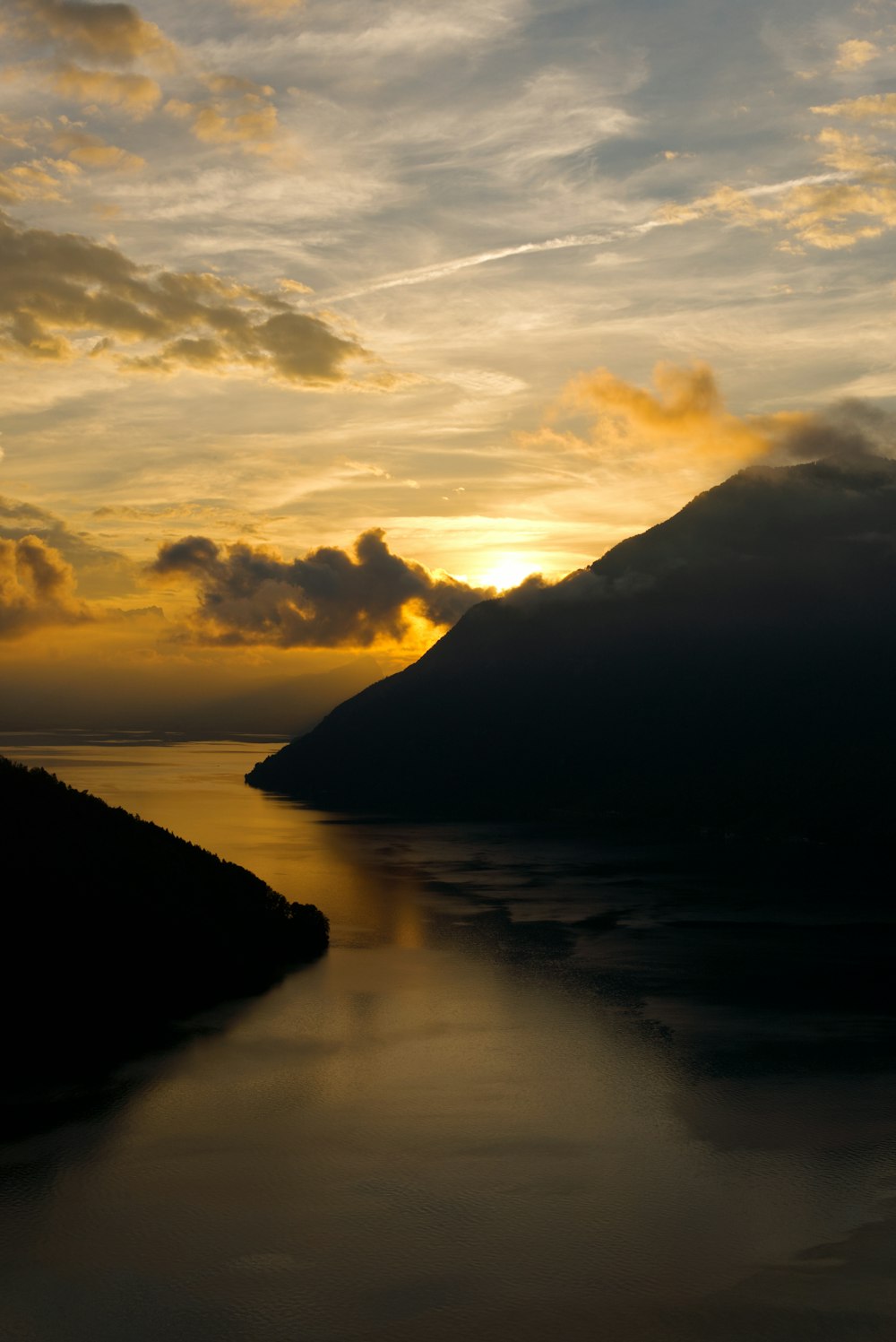 a body of water with a hill and a sunset