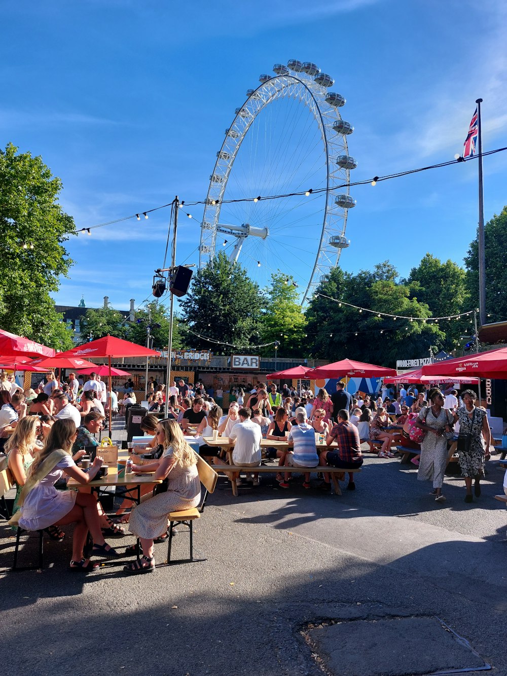 a group of people sitting at tables in front of a ferris wheel