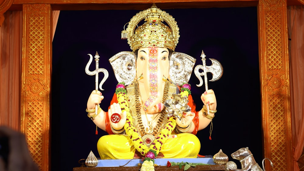 a statue of a person wearing a crown and holding a staff with Venkateswara Temple, Tirumala in the background