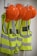 Several bright orange hard hats and fluorescent yellow safety vests with reflective strips are hanging on hooks on a wall.