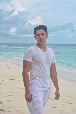 A man wearing a breezy summer shirt and shorts, walking along the shoreline.