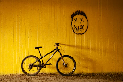 A bicycle against a yellow wall beneath a spray-painted face