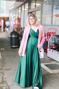A stylish woman wearing an emerald green dress paired with gold accessories, standing confidently in an urban setting.