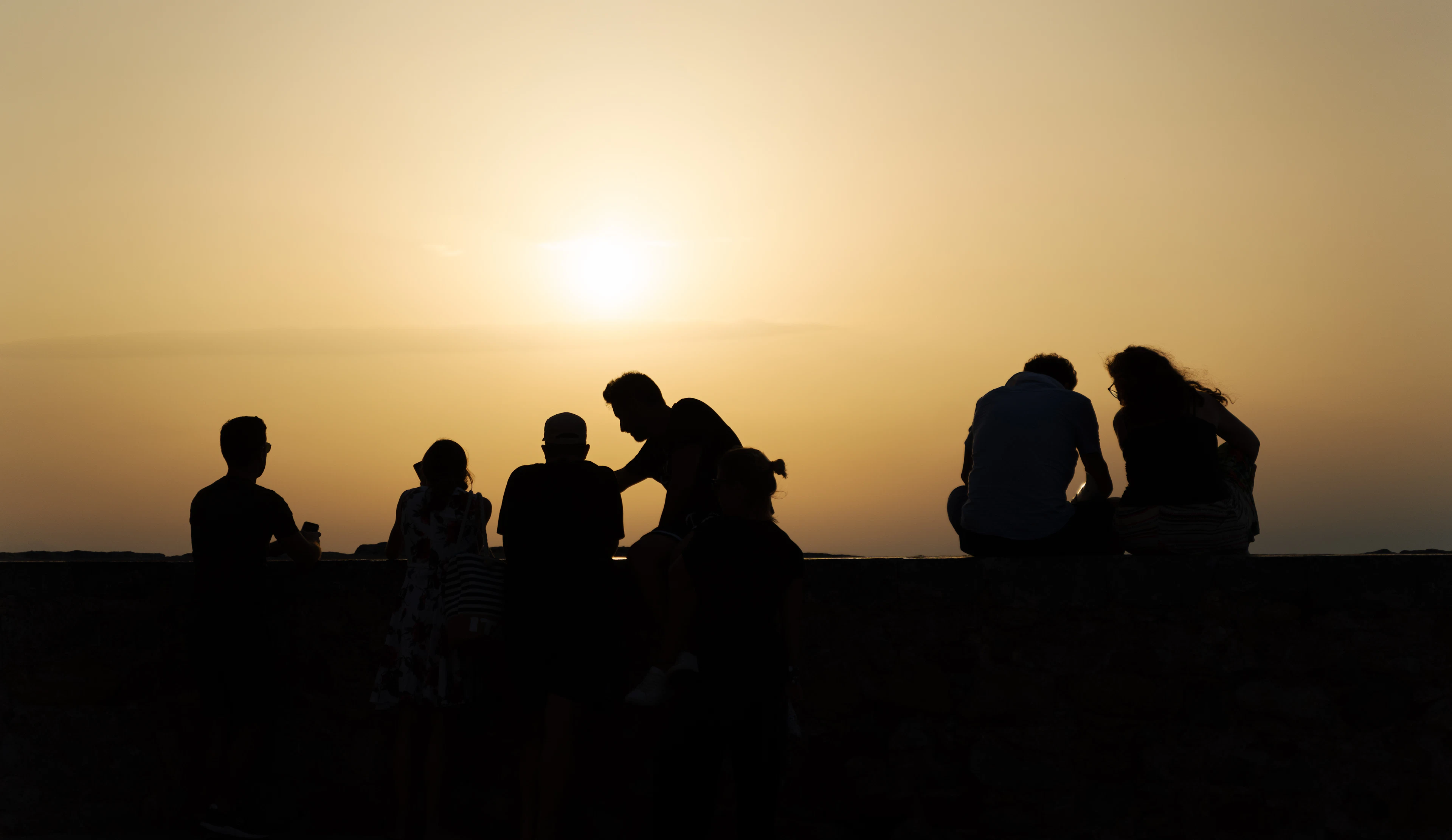 A group of friends sitting together on a bench watching the sunset
