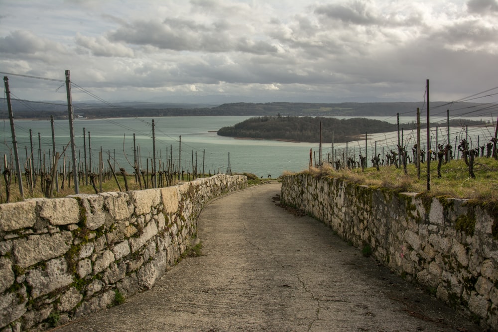a stone path with a stone wall and a body of water in the background