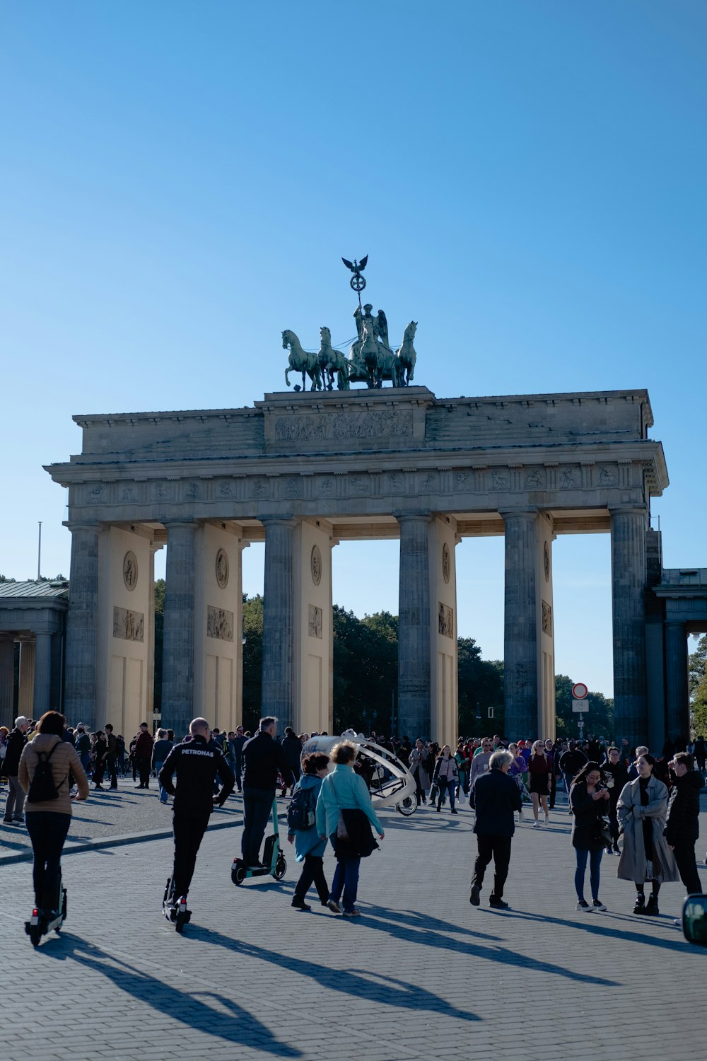 um grande grupo de pessoas andando em frente ao Portão de Brandemburgo com colunas e uma estátua no topo