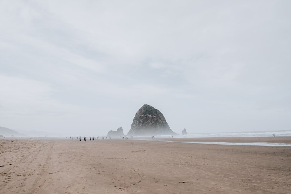 a group of people walking on a beach with a large rock in the distance