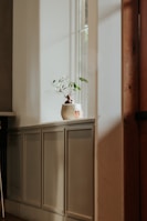 A minimalist room bathed in soft natural light with pale blue walls and a simple plant on the windowsill.