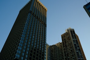 Several tall skyscrapers rise against a clear blue sky, capturing a robust urban skyline with geometric patterns created by windows and structures.