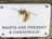 A warning sign is attached to a wooden surface with screws, displaying an illustration of a wasp. The message on the sign reads 'WASPS ARE PRESENT & DANGEROUS' in bold black letters.