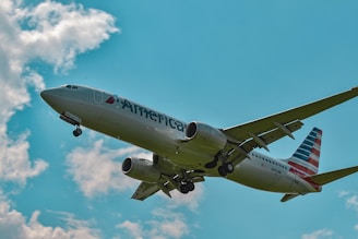 An orange passenger plane soaring smoothly against a clear blue sky with white clouds.