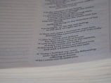 A close-up of a page from a book featuring text that appears to be poetic or scriptural, formatted in a column with verse numbers. The page is slightly curved, and the text is printed in a clear, serif font.