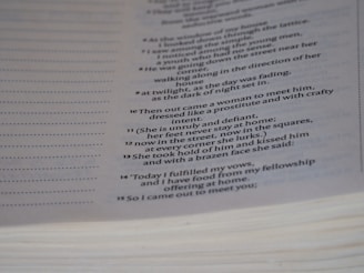 A close-up of a page from a book featuring text that appears to be poetic or scriptural, formatted in a column with verse numbers. The page is slightly curved, and the text is printed in a clear, serif font.