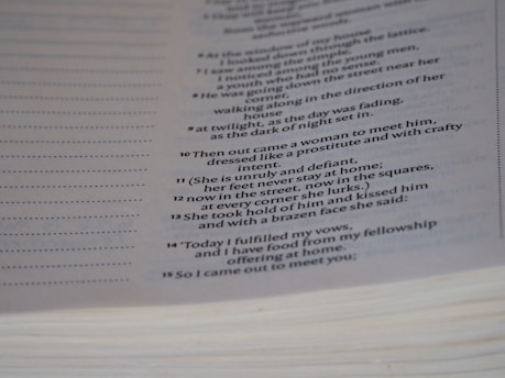 A close-up of a page from a book featuring text that appears to be poetic or scriptural, formatted in a column with verse numbers. The page is slightly curved, and the text is printed in a clear, serif font.