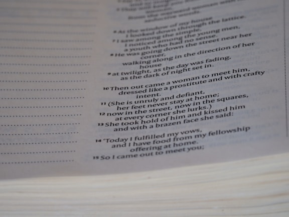 A close-up of a page from a book featuring text that appears to be poetic or scriptural, formatted in a column with verse numbers. The page is slightly curved, and the text is printed in a clear, serif font.