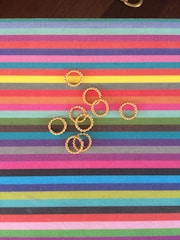 Elegant gold rings displayed on a colorful fabric background.
