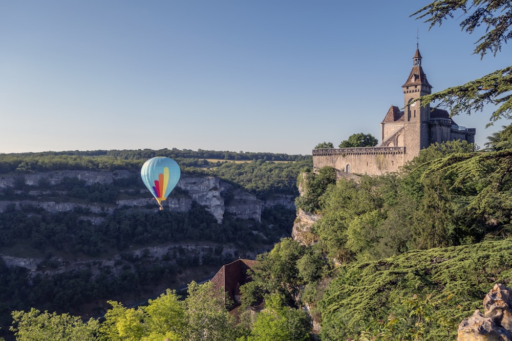 a hot air balloon flying over a hill with trees and a castle