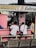 A small eatery with a pink exterior where several people are seated at a counter. The eatery, named 'Mommy J Eatery', is located at a stall and offers special dishes like lomi and silog. Inside, there are various bottles and items on shelves. The seating area includes benches and metal chairs.