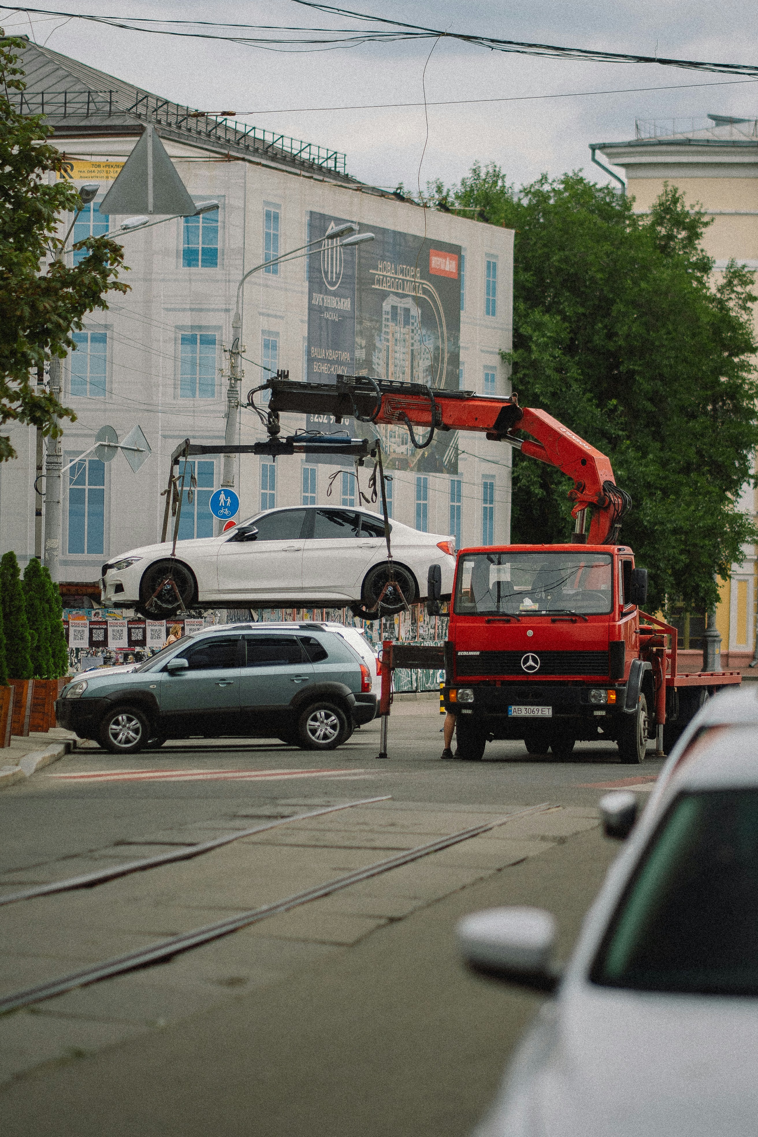A red tow truck lifting a white sedan on city street.