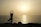 A person is practicing yoga, balanced on one leg with arms raised, silhouetted against a serene sunset over the ocean. The calm sea reflects the warm, golden hues of the setting sun.