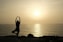 A serene landscape with a person practicing yoga at sunrise.
