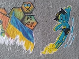A cartoon character resembling a playful, futuristic boy with black hair and a blue and yellow suit is depicted flying with a trail of yellow flames behind him. Next to him are colorful hexagon shapes with a blue heart, a yellow and blue ribbon, and the words 'NO WAR'. A flag with blue and yellow colors is also illustrated, suggesting a message of peace and anti-war sentiment.