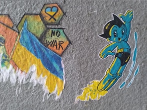 A cartoon character resembling a playful, futuristic boy with black hair and a blue and yellow suit is depicted flying with a trail of yellow flames behind him. Next to him are colorful hexagon shapes with a blue heart, a yellow and blue ribbon, and the words 'NO WAR'. A flag with blue and yellow colors is also illustrated, suggesting a message of peace and anti-war sentiment.