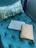 A green tufted cushion is adorned with a patterned pillow and accompanied by a textured laptop sleeve and a brown patterned clutch, all arranged on the cushion.