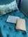 A green tufted cushion is adorned with a patterned pillow and accompanied by a textured laptop sleeve and a brown patterned clutch, all arranged on the cushion.