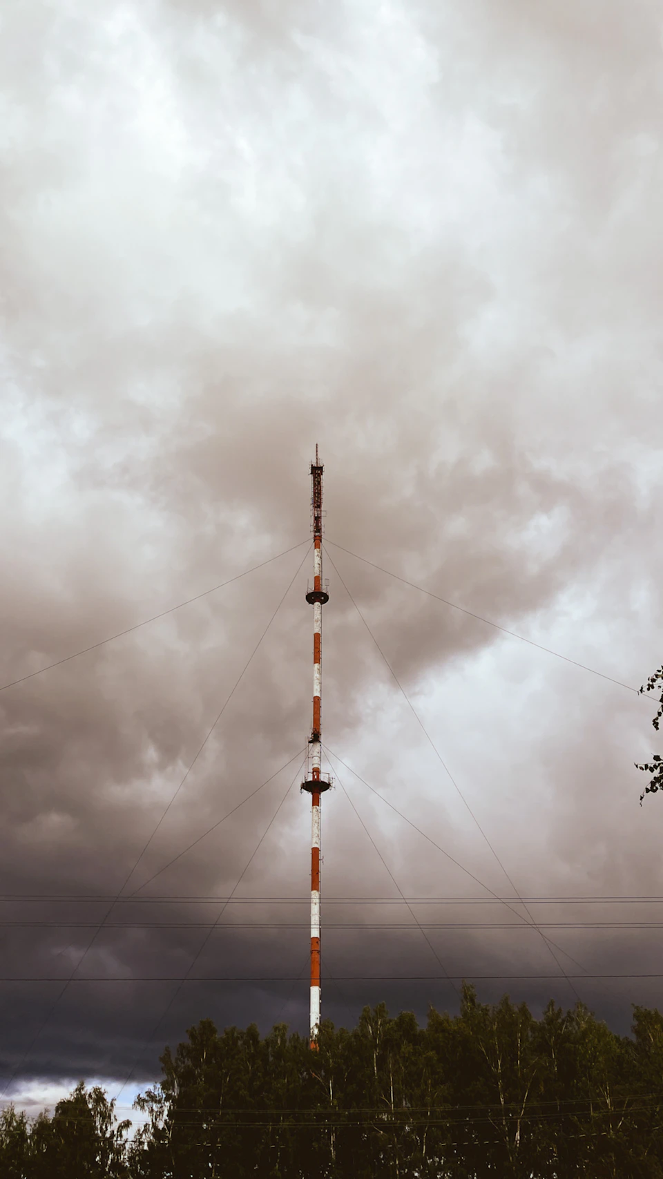 Tall white and orange radio tower stands against overcast sky with dark clouds nearby