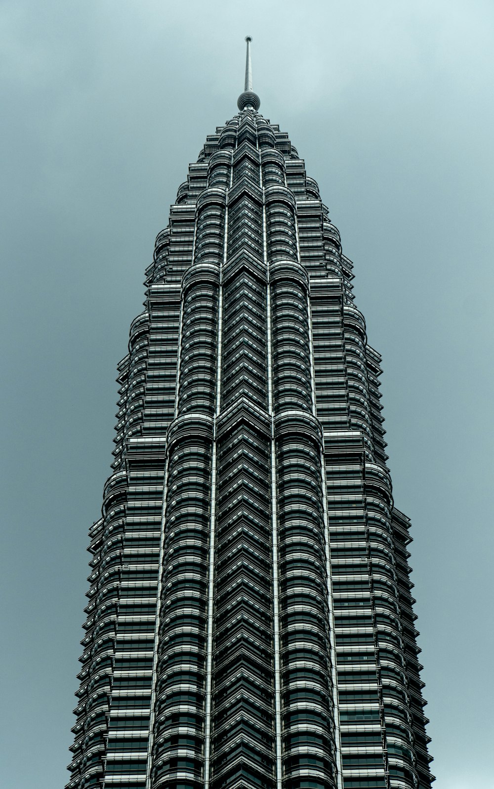 a tall building with a pointy top with Petronas Towers in the background