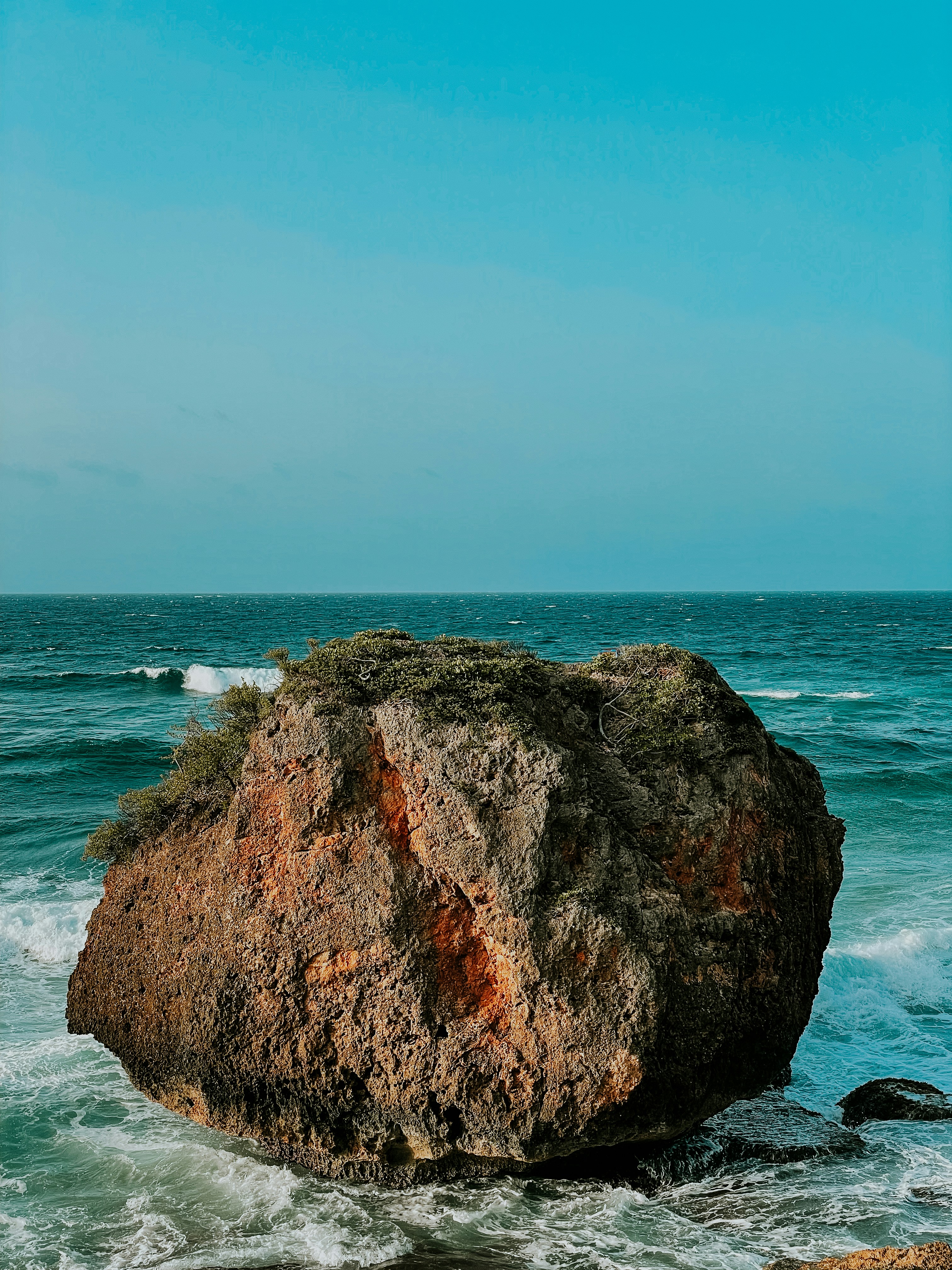 Large coastal rock formation in turquoise waters of Puerto Rico, surrounded by crashing waves against rugged coastline