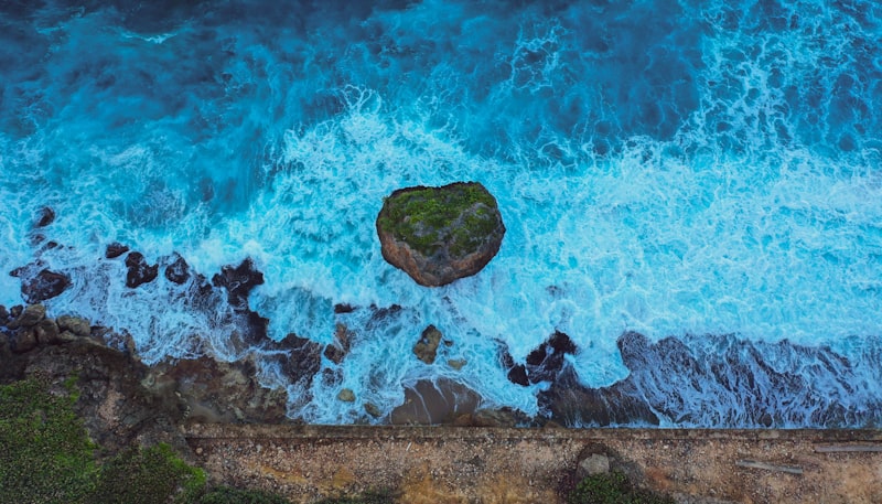 Aerial view of white surf breaking over dark rocks and a lone boulder along a rugged shoreline in Isabela