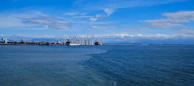 Oceanfront industrial port with cargo ships and cranes under a deep blue sky, symbolizing maritime sector activity.