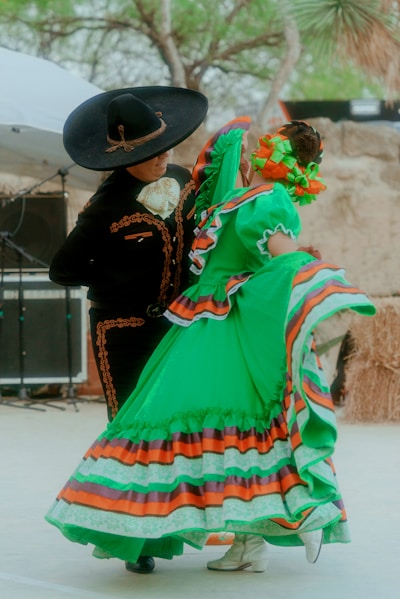 a woman in a colorful dress and hat with a man in a black hat and a black coat