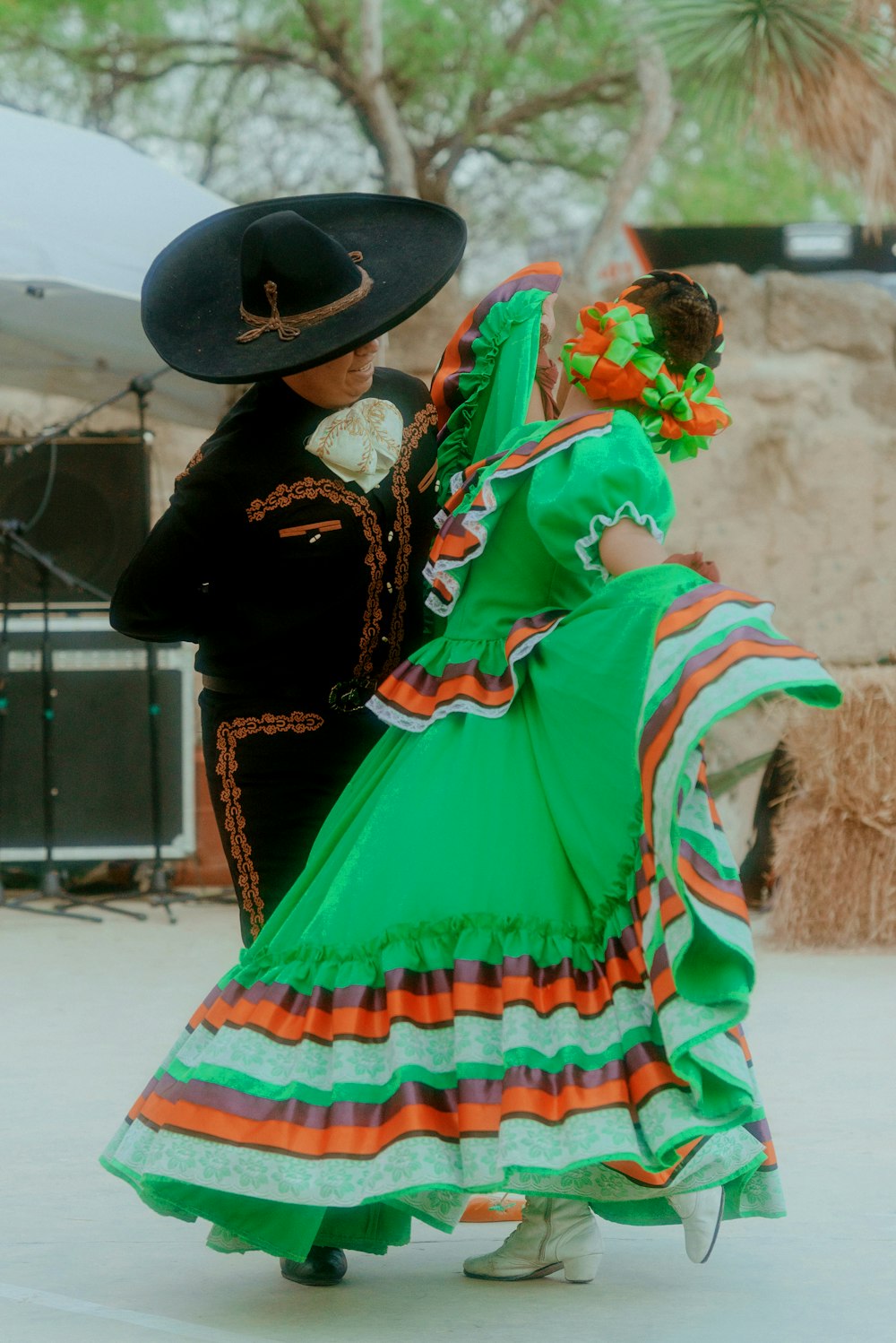 a woman in a colorful dress and hat with a man in a black hat and a black coat