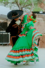 a woman in a colorful dress and hat with a man in a black hat and a black coat