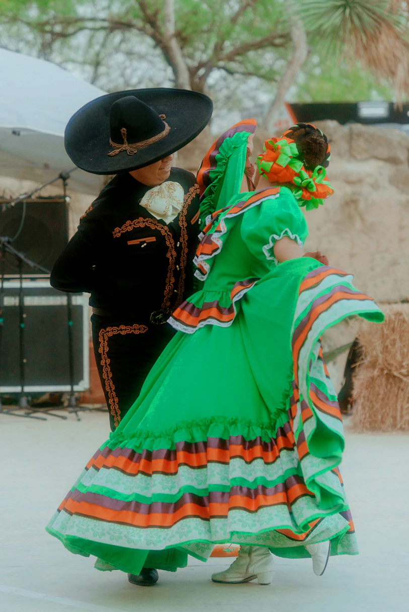 a woman in a colorful dress and hat with a man in a black hat and a black coat