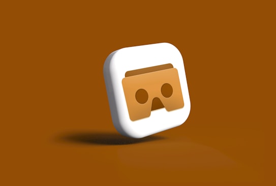 A three-dimensional icon featuring a stylized pair of VR goggles in the center. The goggles appear in a brownish shade on a square-shaped background with smooth, rounded edges. The icon is set against a monochromatic brown backdrop, enhancing the visual focus on the goggles.