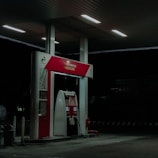 A dimly lit petrol station at night featuring a single fuel pump with the labels Pertamax 92 and Pertalite. The atmosphere is quiet with minimal lighting coming from overhead lights.