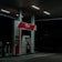 A dimly lit petrol station at night featuring a single fuel pump with the labels Pertamax 92 and Pertalite. The atmosphere is quiet with minimal lighting coming from overhead lights.