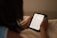 A person is holding an e-reader device, reading text from it. The background is soft and out of focus, giving a cozy and calm ambiance.