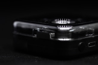 A close-up view reveals part of a clear, plastic-cased electronic device with a circular array of white LED lights. The focus is on the device's corner, highlighting intricate details such as small connectors and buttons.