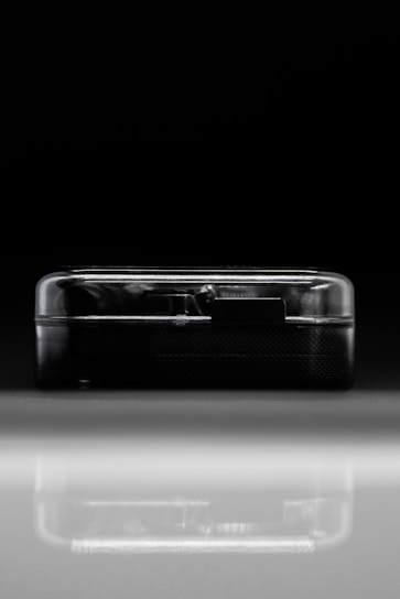 A compact, semi-transparent black rectangular device is placed against a dark background and reflects on a shiny surface. The sleek lines and minimalist design suggest modern technology.